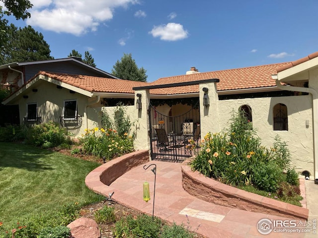 back of house featuring a yard, stucco siding, a tile roof, and a patio