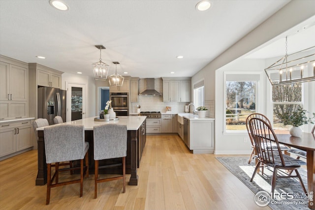 kitchen featuring a kitchen island, stainless steel appliances, light countertops, wall chimney exhaust hood, and backsplash