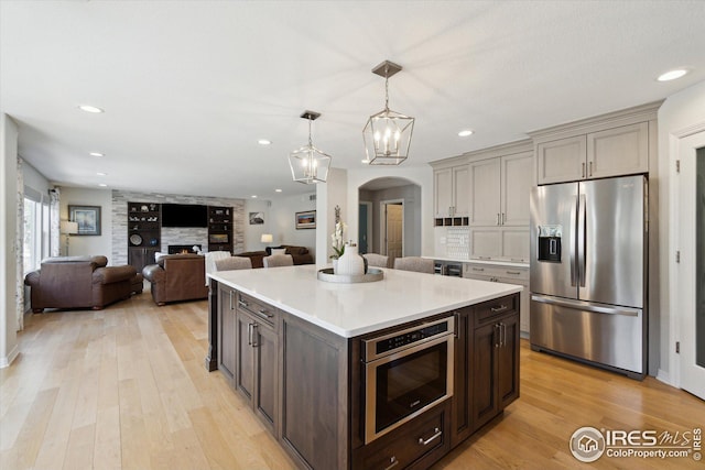 kitchen with light wood-style flooring, arched walkways, a large fireplace, stainless steel fridge with ice dispenser, and built in microwave