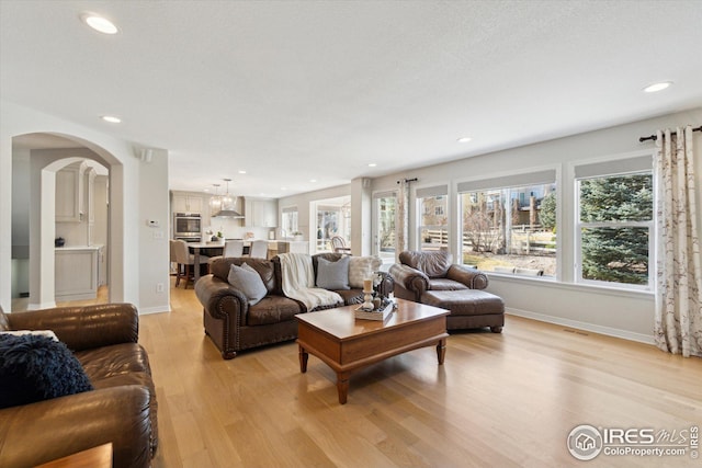 living area featuring recessed lighting, baseboards, arched walkways, and light wood finished floors