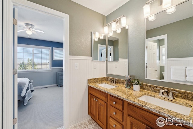 bathroom featuring a sink, a ceiling fan, double vanity, and wainscoting