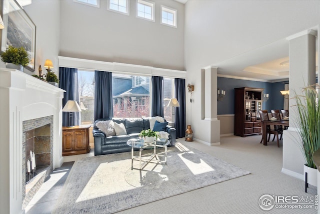 carpeted living room with a tiled fireplace, baseboards, a towering ceiling, and ornamental molding