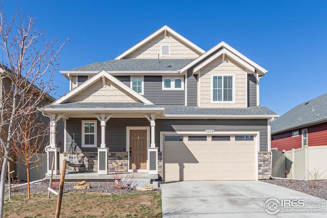 craftsman-style home featuring stone siding, a porch, fence, roof with shingles, and concrete driveway