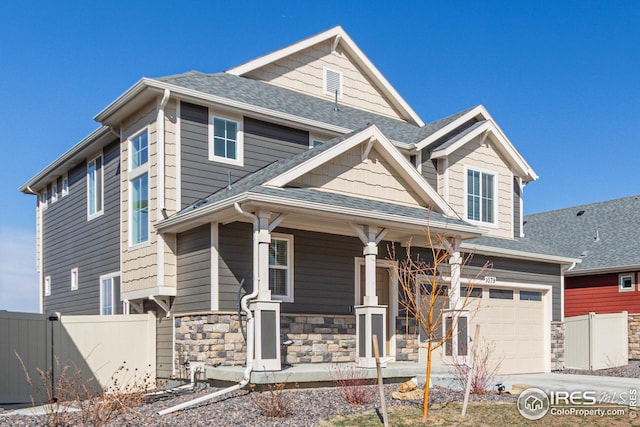 view of front facade featuring stone siding, a porch, an attached garage, and fence