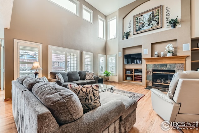 living room with a fireplace, light wood finished floors, plenty of natural light, and a towering ceiling