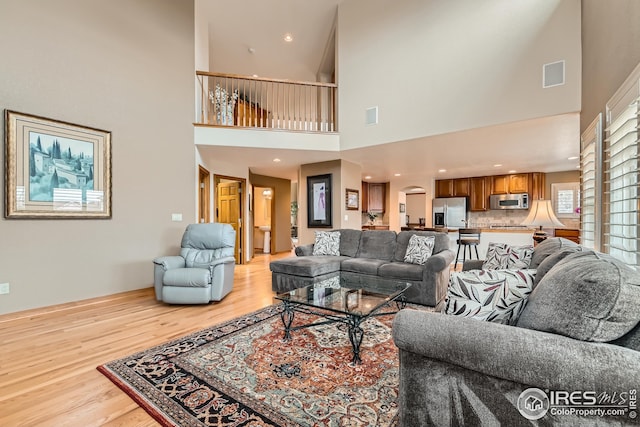 living area with visible vents, light wood finished floors, and a towering ceiling