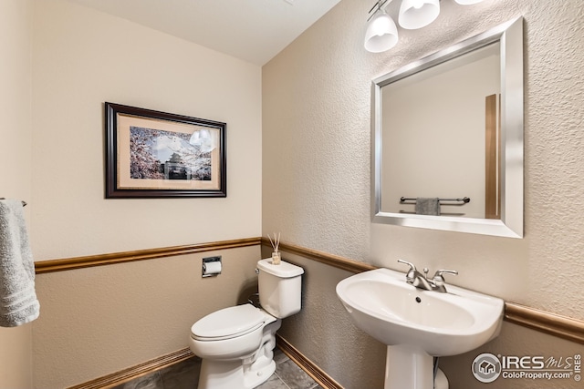 half bath featuring toilet, a textured wall, and a sink