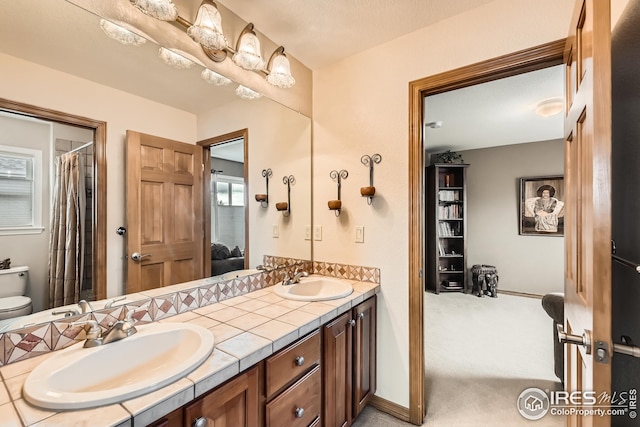 bathroom featuring double vanity, ensuite bath, toilet, and a sink