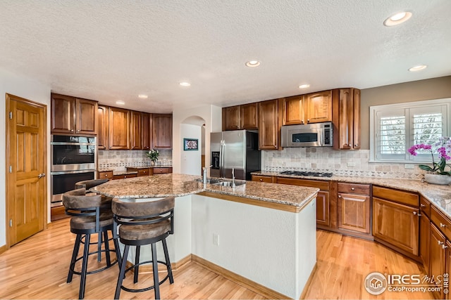 kitchen featuring stainless steel appliances, light wood-style floors, a center island with sink, tasteful backsplash, and a textured ceiling