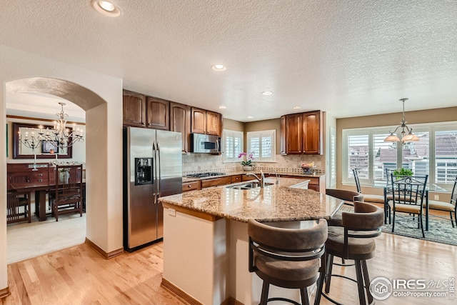 kitchen with arched walkways, a notable chandelier, stainless steel appliances, and a sink