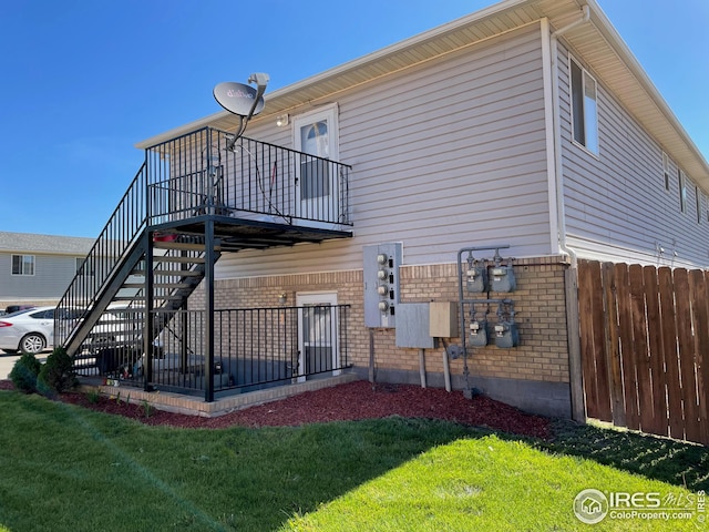 view of side of property featuring a yard, fence, brick siding, and stairway