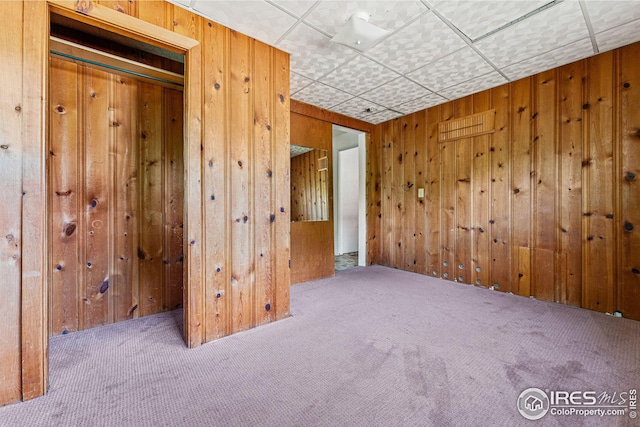 empty room featuring wooden walls, carpet, and a drop ceiling