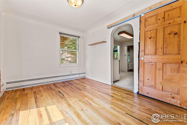 spare room featuring light wood-style floors, arched walkways, and baseboard heating