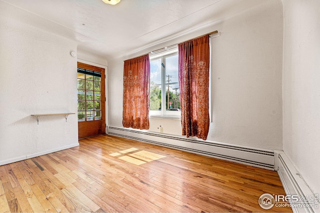 empty room with hardwood / wood-style flooring, a healthy amount of sunlight, and baseboard heating