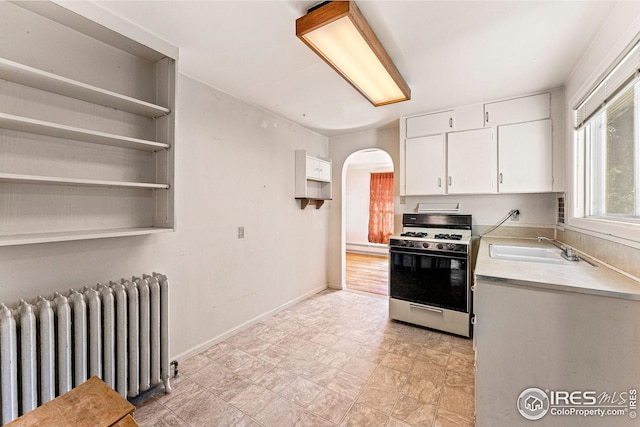 kitchen with radiator heating unit, white cabinetry, arched walkways, light countertops, and gas range