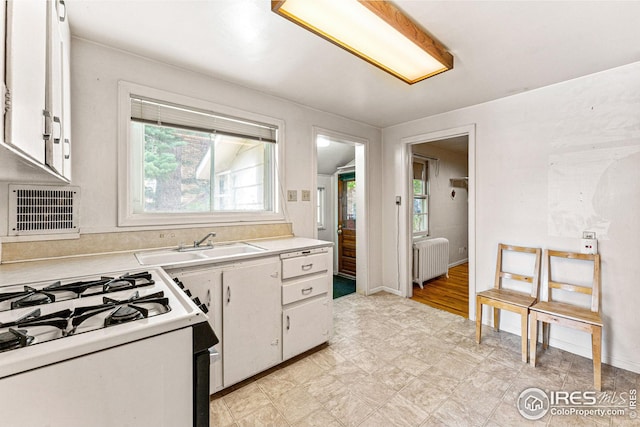 kitchen featuring radiator, white range with gas stovetop, light countertops, white cabinets, and a sink