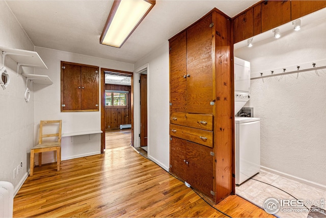 clothes washing area with light wood finished floors, baseboard heating, stacked washing maching and dryer, and baseboards