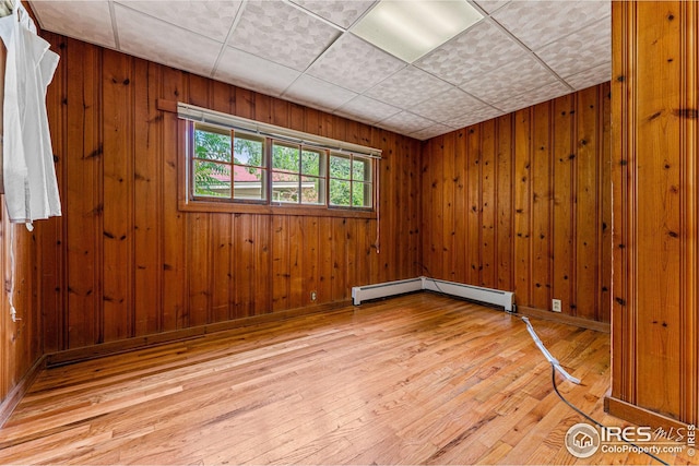 unfurnished room with light wood-type flooring, a drop ceiling, wooden walls, baseboards, and baseboard heating