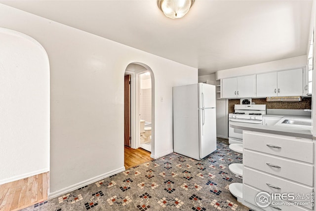 kitchen with white appliances, baseboards, arched walkways, a sink, and white cabinetry