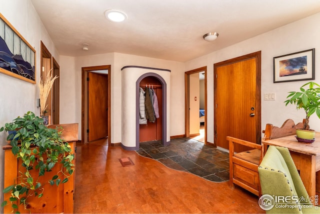 foyer with baseboards, arched walkways, and dark wood-style flooring