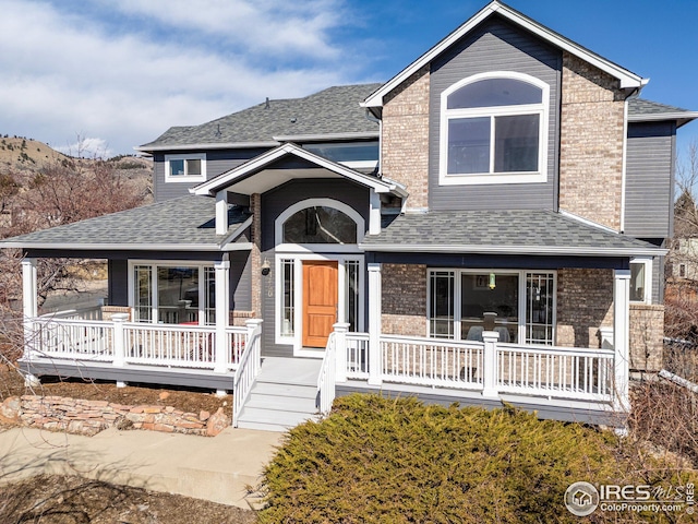 view of front of home with brick siding, covered porch, and a shingled roof