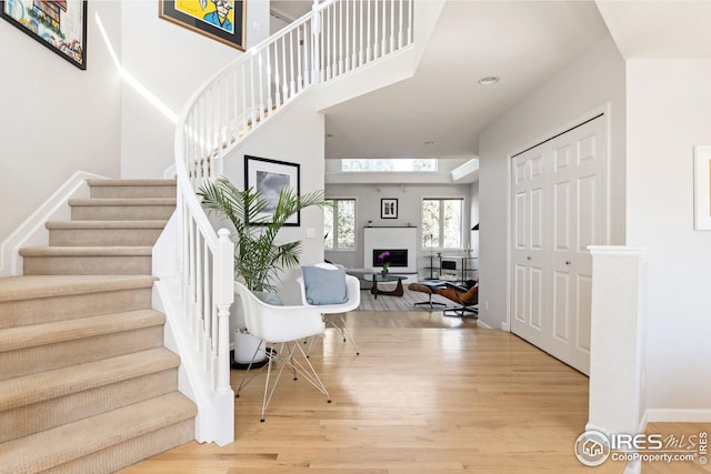 stairway with a fireplace, wood finished floors, baseboards, and a towering ceiling