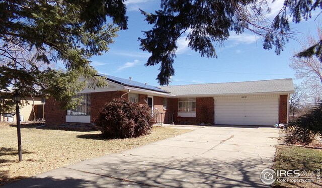 ranch-style home featuring roof mounted solar panels, brick siding, an attached garage, and driveway