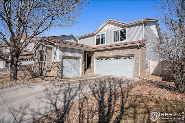 traditional home featuring a garage, a tile roof, concrete driveway, and brick siding