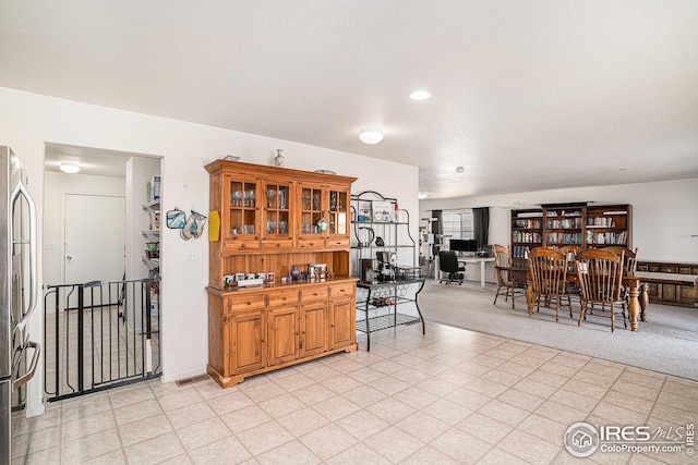 kitchen featuring glass insert cabinets, brown cabinetry, light carpet, and freestanding refrigerator