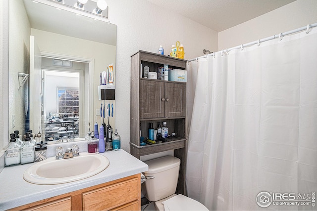 bathroom featuring visible vents, toilet, curtained shower, vanity, and a textured wall