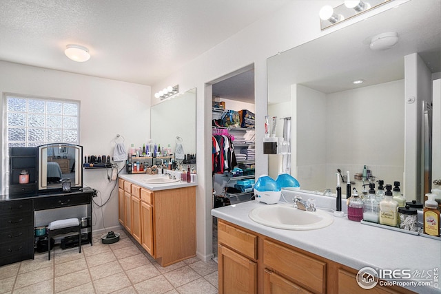 bathroom with a walk in closet, a textured ceiling, two vanities, and a sink