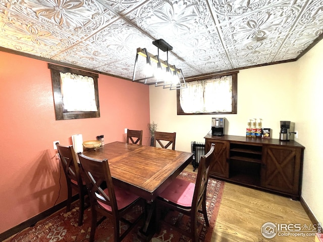 dining room featuring radiator, wood finished floors, baseboards, and an ornate ceiling