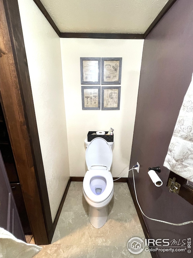 bathroom with baseboards, toilet, concrete flooring, and crown molding