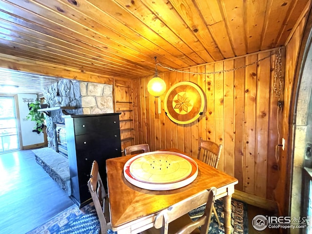 dining area featuring a stone fireplace, wood walls, wood ceiling, and wood finished floors