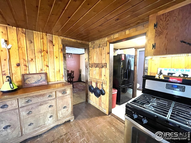 kitchen with wood walls, dark wood-style floors, wooden ceiling, stainless steel gas range, and black fridge