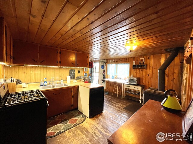 kitchen with a sink, black range with gas cooktop, wood finished floors, and wood walls