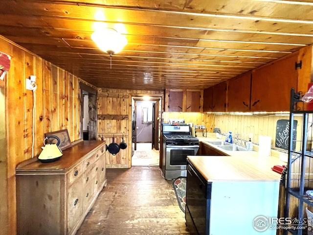 kitchen with a sink, fridge, light countertops, stainless steel gas stove, and wooden walls