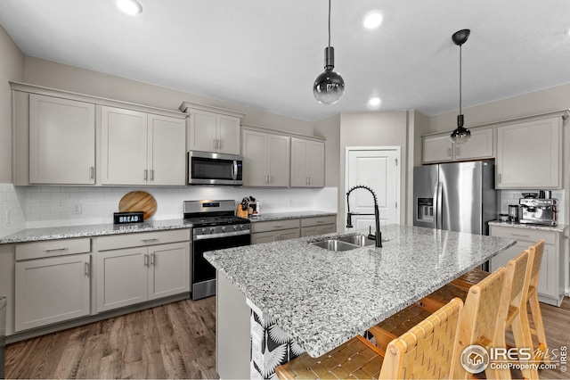 kitchen with a breakfast bar, decorative backsplash, appliances with stainless steel finishes, wood finished floors, and a sink