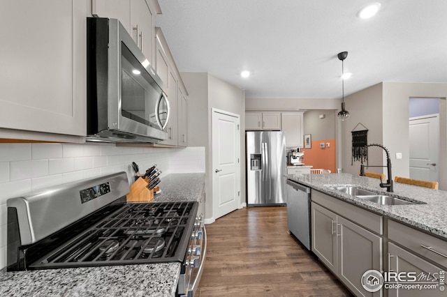 kitchen featuring light stone counters, dark wood finished floors, a sink, decorative backsplash, and appliances with stainless steel finishes