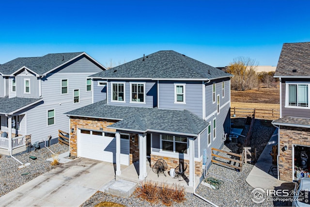 traditional-style house featuring fence, roof with shingles, an attached garage, concrete driveway, and stone siding