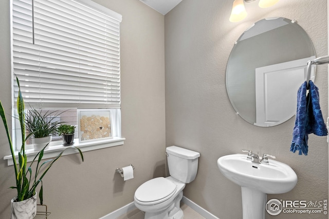 half bathroom with a sink, baseboards, and toilet