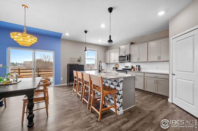 kitchen featuring backsplash, dark wood-style flooring, appliances with stainless steel finishes, a kitchen breakfast bar, and a kitchen island with sink