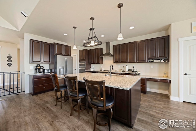 kitchen with dark brown cabinetry, appliances with stainless steel finishes, dark wood-style floors, wall chimney exhaust hood, and a sink