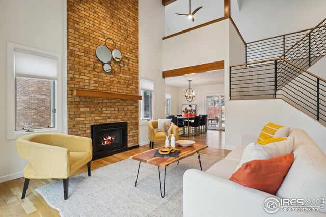 living area with a brick fireplace, stairs, a high ceiling, an inviting chandelier, and wood finished floors