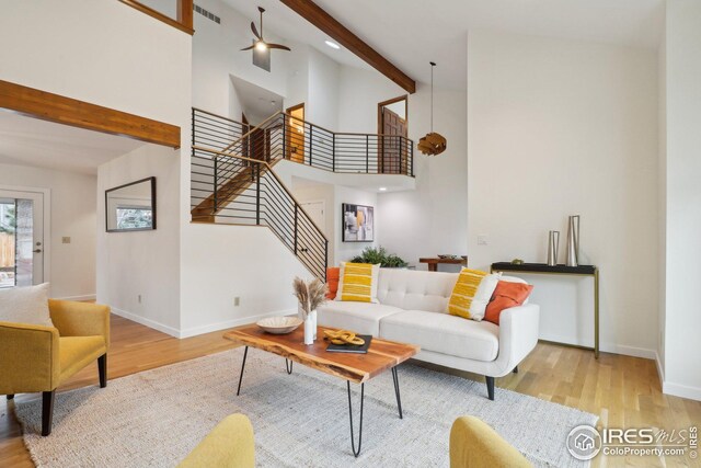 living room featuring beam ceiling, high vaulted ceiling, wood finished floors, stairway, and baseboards