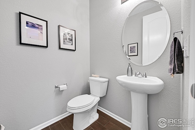 bathroom featuring toilet, a textured wall, baseboards, and wood finish floors