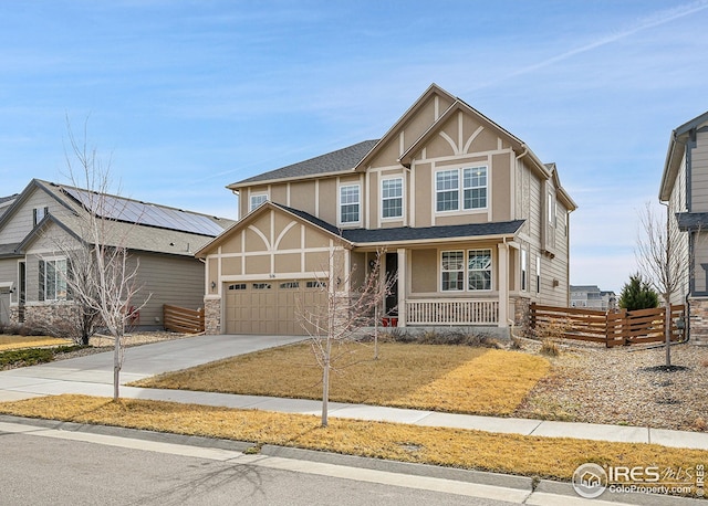 tudor-style house featuring stucco siding, a shingled roof, concrete driveway, and fence