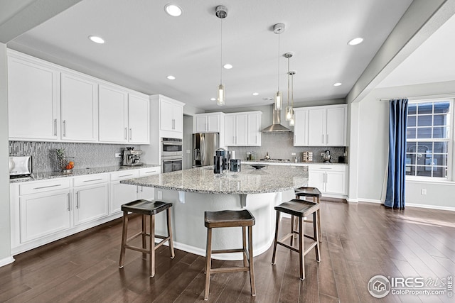 kitchen with dark wood finished floors, a kitchen island with sink, appliances with stainless steel finishes, white cabinetry, and wall chimney exhaust hood