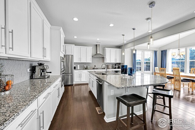 kitchen with stainless steel dishwasher, wall chimney range hood, dark wood finished floors, and a sink