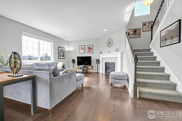 living area with dark wood-type flooring, a tiled fireplace, recessed lighting, baseboards, and stairs